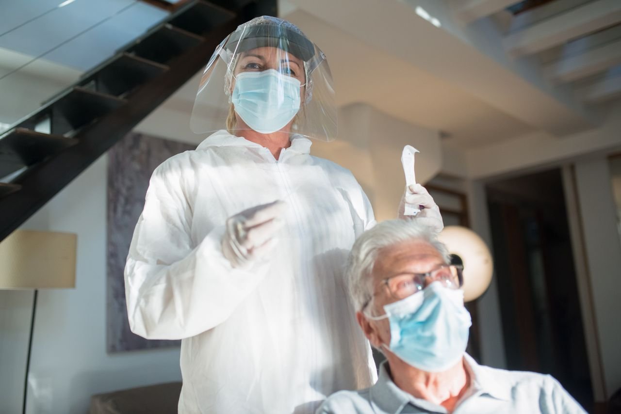 Healthcare professional in protective gear assisting elderly patient in a modern setting.