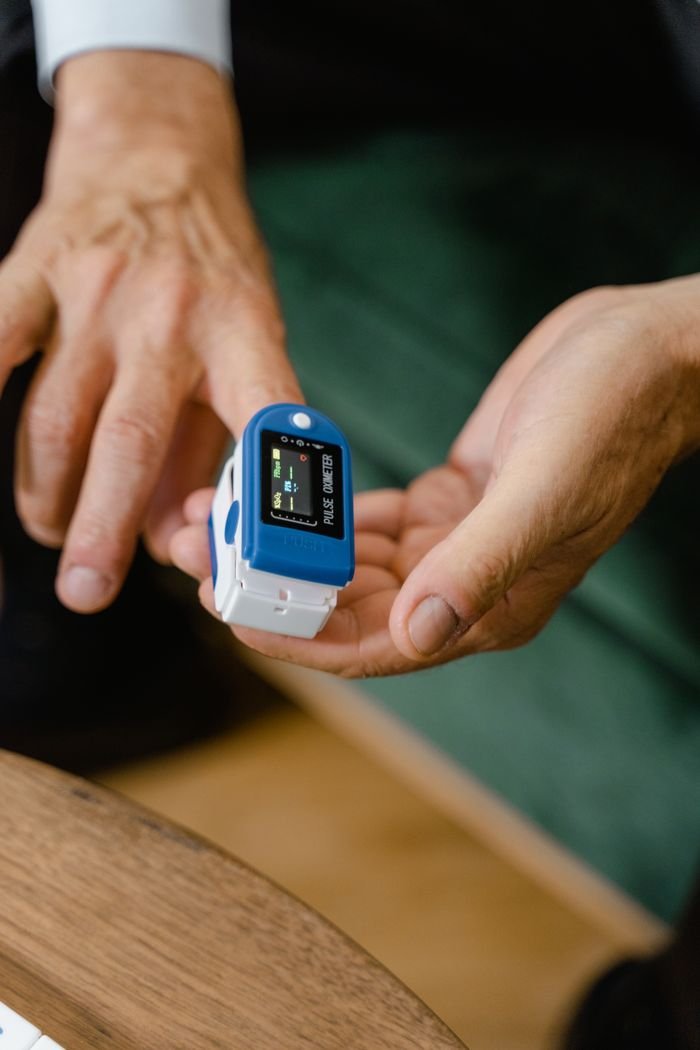 Hands of an adult using a pulse oximeter device to measure oxygen levels indoors.