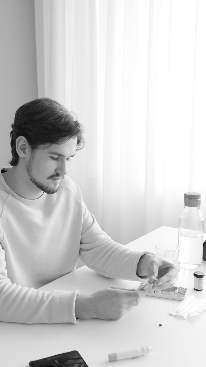 A young adult checking blood glucose levels using a glucometer at home in grayscale.